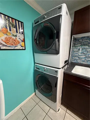 Dedicated laundry area featuring a stacked washer and dryer unit, a utility sink with a tiled backsplash, dark wood-finish cabinetry, and light-toned floor tiling