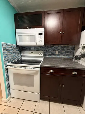 Kitchen workspace featuring a white electric range, white over-the-range microwave, dark wood-finish cabinetry, and a mosaic tile backsplash