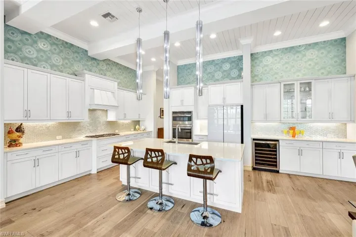 Kitchen featuring white cabinets, light wood-type flooring, a center island with sink, and beverage cooler