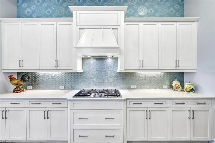 Kitchen featuring white cabinets, backsplash, custom exhaust hood, and stainless steel gas stovetop