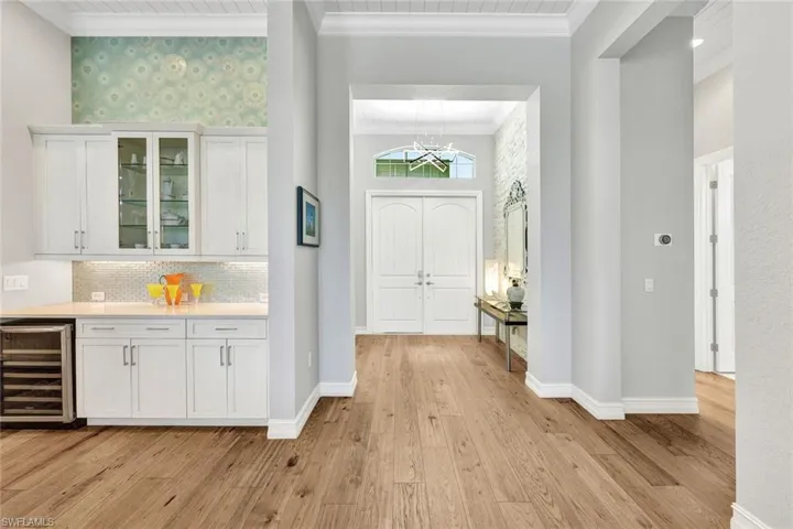 Entryway featuring an inviting chandelier, light, stone accent wall, hardwood / wood-style flooring, beverage cooler, and crown molding