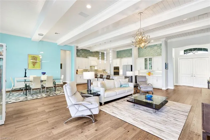 Living room featuring light wood-style floors, a notable chandelier, molding, and beam ceiling