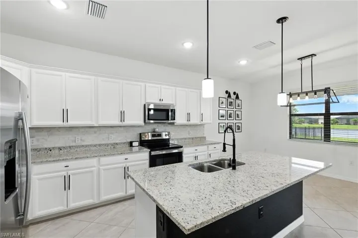Kitchen with light tile patterned floors, appliances with stainless steel finishes, tasteful backsplash, white cabinets, and hanging light fixtures