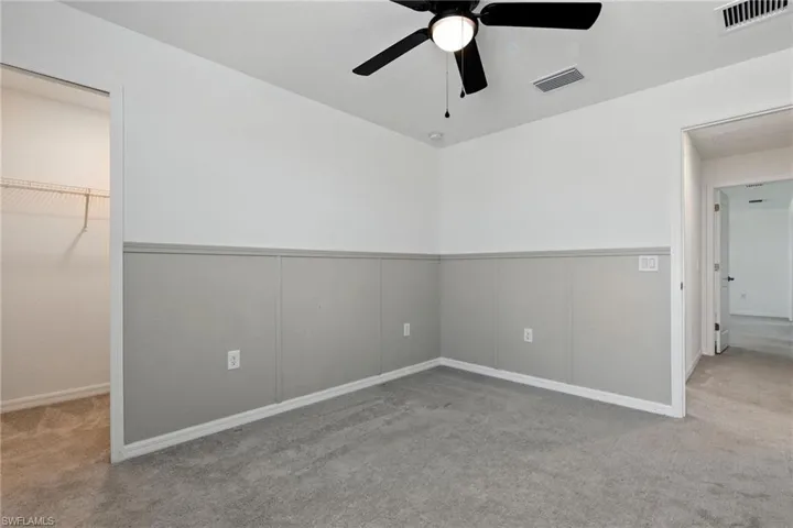 Unfurnished bedroom with carpet, a wainscoted wall, and a ceiling fan