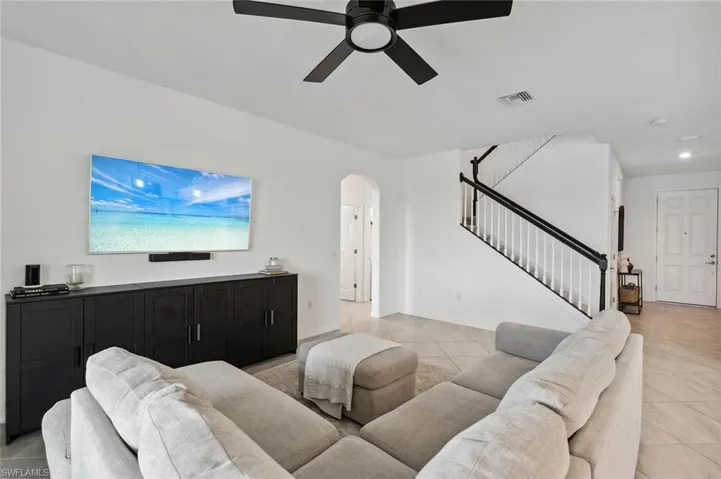 Living room featuring light tile patterned floors, arched walkways, stairs, a ceiling fan, and recessed lighting