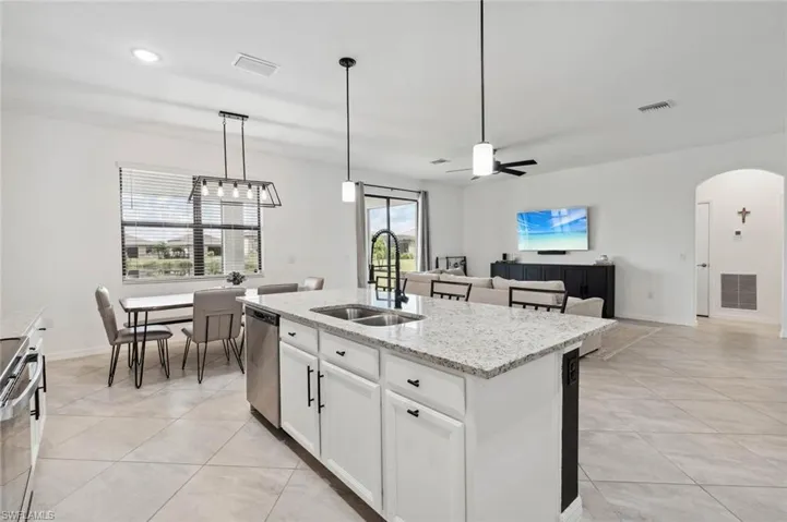 Kitchen with light stone countertops, hanging light fixtures, white cabinetry, ceiling fan, and open floor plan