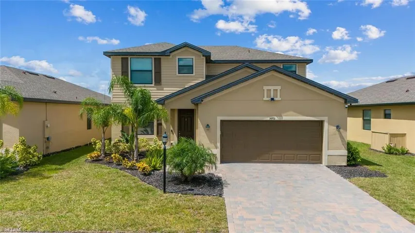 Traditional-style house featuring a front yard, decorative driveway, stucco siding, and an attached garage