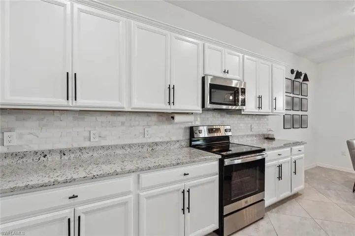 Kitchen with stainless steel appliances, light stone counters, white cabinetry, light tile patterned floors, and decorative backsplash