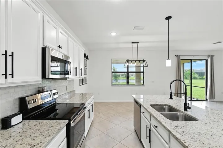 Kitchen featuring stainless steel appliances, tasteful backsplash, white cabinetry, light tile patterned flooring, and decorative light fixtures