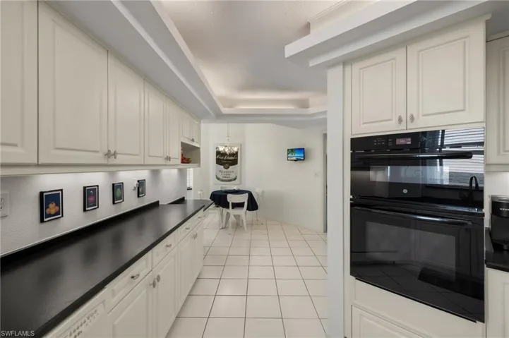 Kitchen featuring light tile patterned floors, dark countertops, a tray ceiling, and white cabinetry