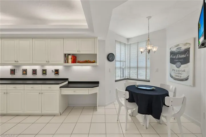 Kitchen featuring dark countertops, white cabinets, a chandelier, light tile patterned flooring, and pendant lighting