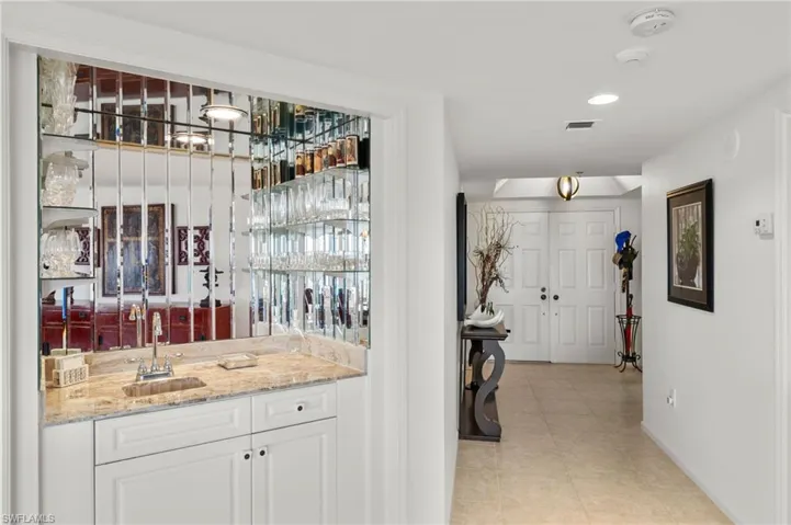 Indoor wet bar featuring white cabinets, light stone countertops, recessed lighting, and light tile patterned floors