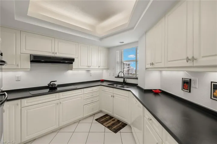 Kitchen featuring a raised ceiling, dark countertops, light tile patterned floors, and under cabinet range hood