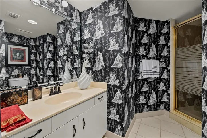 Full bath with wallpapered walls, light tile patterned flooring, vanity, and a shower stall