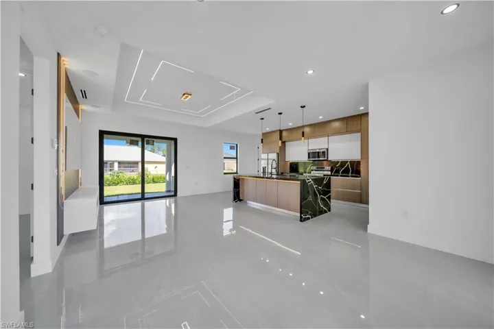 Two tone kitchen with modern cabinets, open floor plan, a kitchen island with sink, pendant lighting, and stainless steel microwave