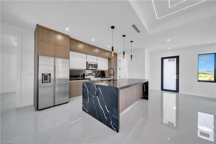 Kitchen with stainless steel appliances, decorative light fixtures, a center island with sink, modern cabinets, and a breakfast bar