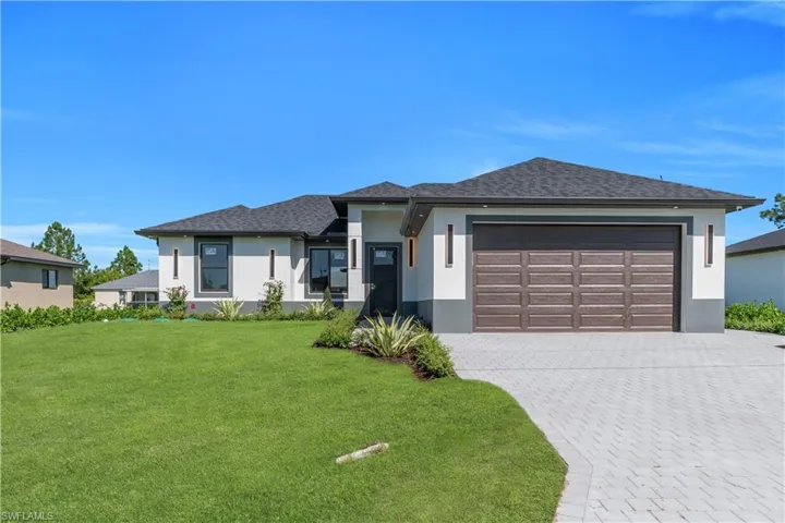 Prairie-style house with stucco siding, a front yard, decorative driveway, an attached garage, and a shingled roof