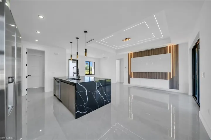 Kitchen with modern cabinets, dark stone counters, stainless steel appliances, decorative light fixtures, and a center island with sink