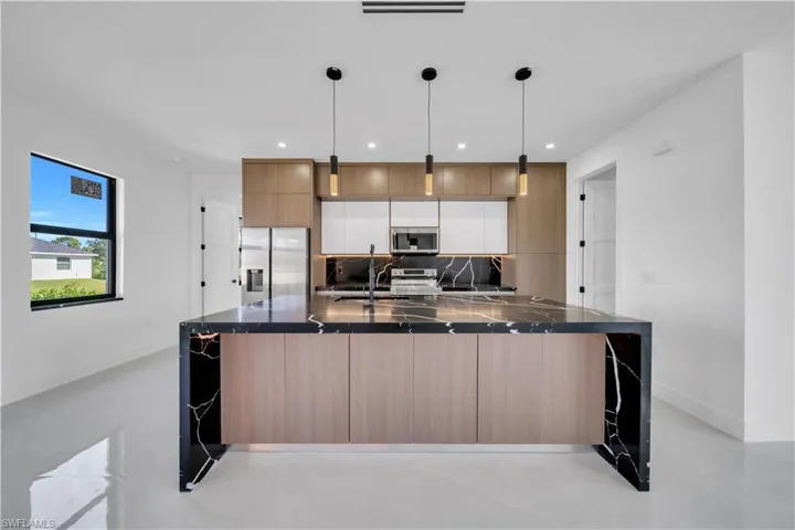 Kitchen with modern cabinets, dark stone counters, stainless steel appliances, decorative light fixtures, and a center island with sink