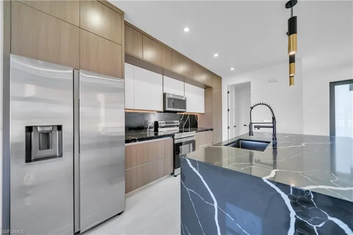Kitchen with stainless steel appliances, hanging light fixtures, dark stone counters, modern cabinets, and two tone cabinetry