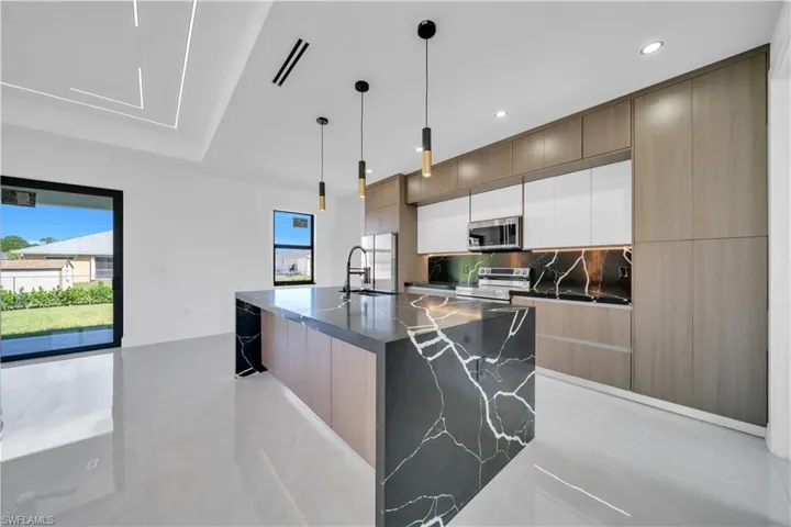Dual tone kitchen with dual tone cabinets, an island with sink, modern cabinets, dark stone countertops, and hanging light fixtures