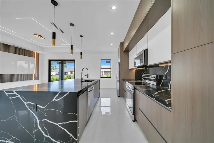 Kitchen with stainless steel appliances, a large island with sink, decorative light fixtures, modern cabinets, and two tone cabinetry