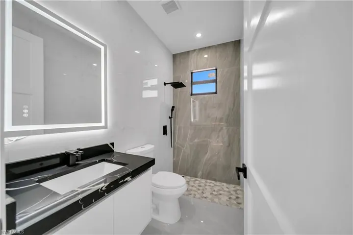 Bathroom with tiled shower, vanity, and recessed lighting
