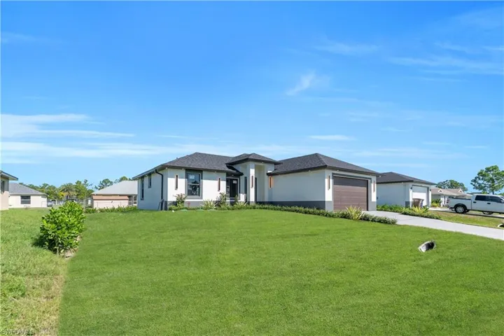 Prairie-style house featuring stucco siding, a front lawn, concrete driveway, and an attached garage