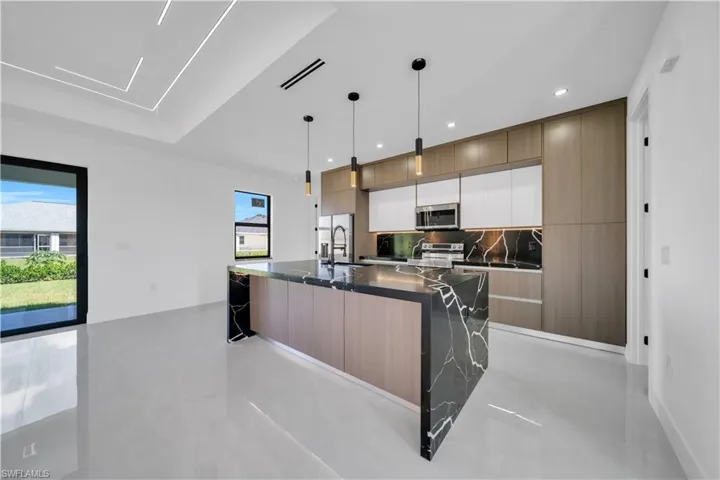 Kitchen featuring two tone cabinetry, a center island with sink, modern cabinets, concrete flooring, and healthy amount of natural light
