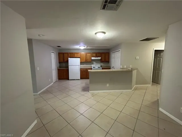 Kitchen with brown cabinetry, light tile patterned floors, a peninsula, white appliances, and light countertops