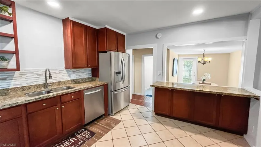 Kitchen featuring stainless steel appliances, decorative light fixtures, sink, and light stone counters