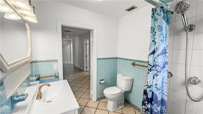 Bathroom with a shower with curtain, vanity, tile walls, tile patterned flooring, and toilet