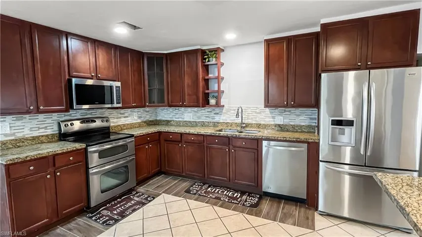 Main Kitchen with sink, light stone counters, stainless steel appliances, backsplash, and hardwood / wood-style flooring