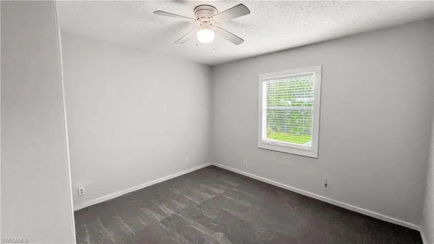 Spare room featuring ceiling fan, a textured ceiling, and dark colored carpet