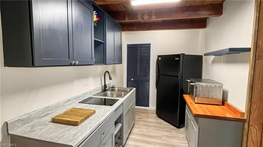 Appartment kitchen with light wood-type flooring, beam ceiling, wood ceiling, sink, and black appliances