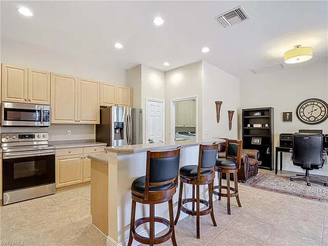 Kitchen featuring stainless steel appliances, light countertops, a kitchen breakfast bar, light wood finish cabinetry, and a desk nook