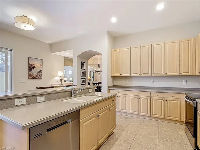 Kitchen with stainless appliances, arched walkways, recessed lighting, and an island with sink