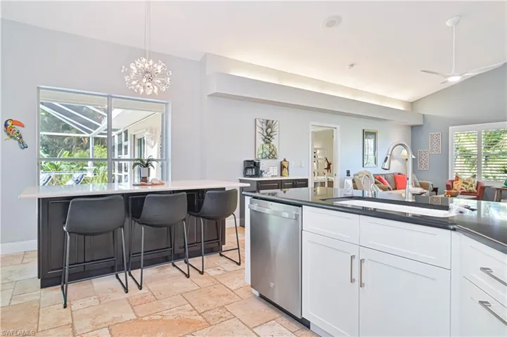 Dual tone kitchen featuring stainless steel dishwasher, ceiling fan, stone tile floors, vaulted ceiling, and dark stone counters