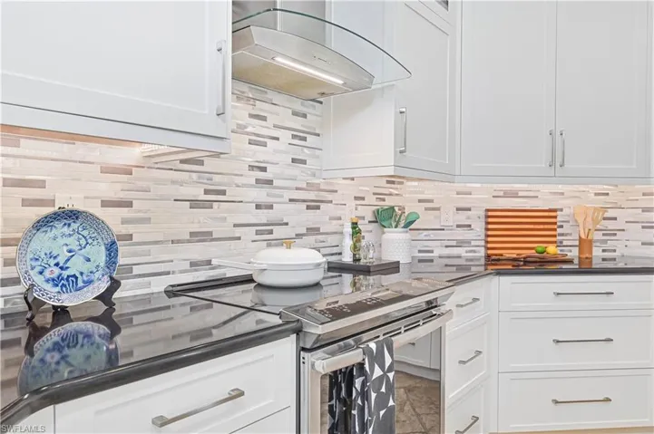 Kitchen featuring stainless steel range with electric stovetop, extractor fan, backsplash, and white cabinets