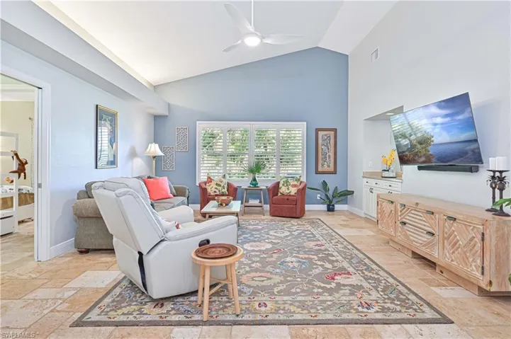 Living area featuring ceiling fan, stone tile flooring, and lofted ceiling