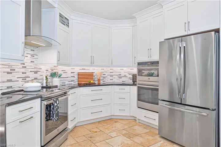 Kitchen with stainless steel appliances, white cabinets, stone tile floors, and backsplash