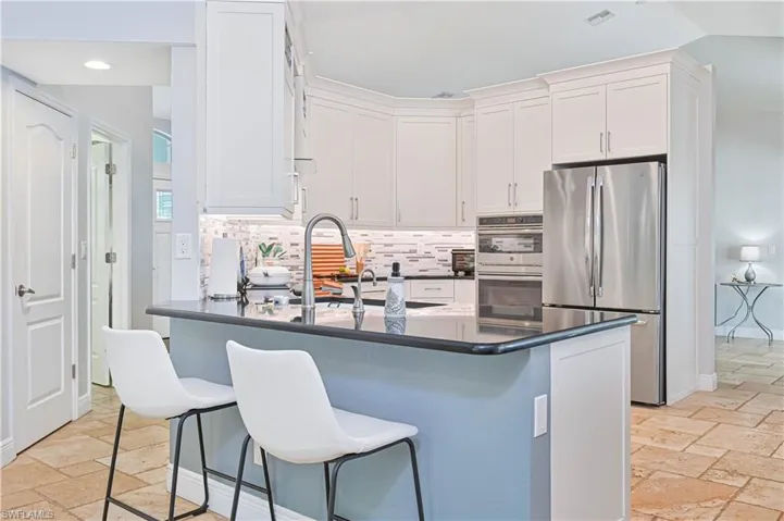 Kitchen with stone tile floors, stainless steel appliances, white cabinetry, a peninsula, and recessed lighting