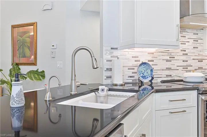 Kitchen with stainless steel electric range, white cabinets, decorative backsplash, and dark stone countertops