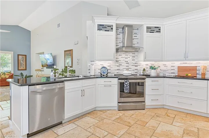 Kitchen featuring stainless steel appliances, vaulted ceiling, white cabinets, and stone tile flooring