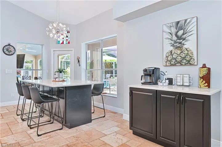 Kitchen with dark cabinetry, light stone counters, a breakfast bar, a center island, and a chandelier