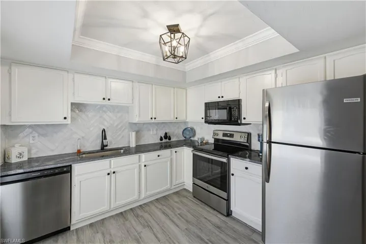 Kitchen with appliances with stainless steel finishes, a raised ceiling, ornamental molding, backsplash, and dark stone counters