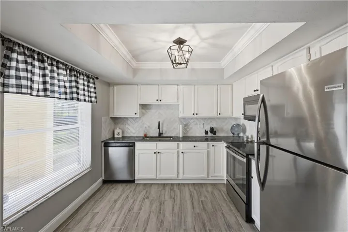 Kitchen with dark countertops, stainless steel appliances, a raised ceiling, crown molding, and tasteful backsplash