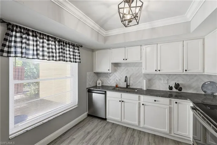 Kitchen featuring dark stone countertops, crown molding, backsplash, white cabinetry, and stainless steel appliances
