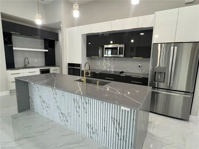 Kitchen featuring appliances with stainless steel finishes, a kitchen island with sink, backsplash, pendant lighting, and sink