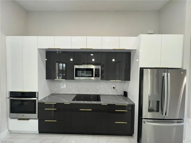 Kitchen with light tile flooring, backsplash, white cabinetry, and appliances with stainless steel finishes